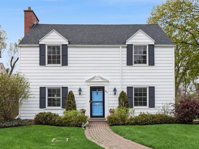 view of front of house with a chimney, a front yard, and a shingled roof