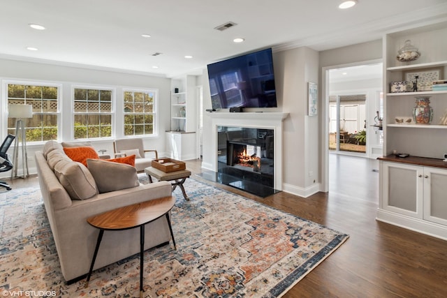living room with a fireplace with flush hearth, dark wood-style flooring, built in features, recessed lighting, and ornamental molding
