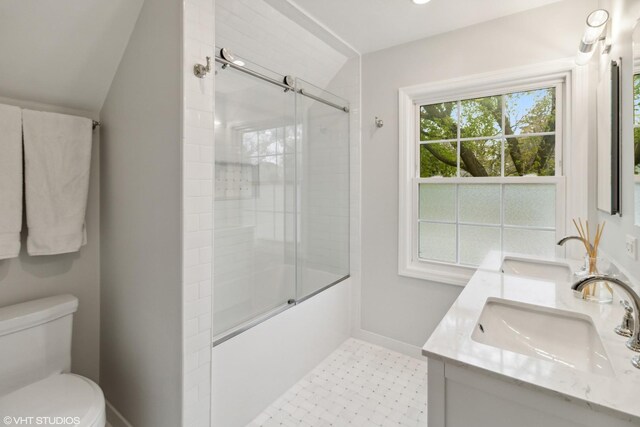 bathroom featuring toilet, vaulted ceiling, baseboards, double vanity, and bath / shower combo with glass door