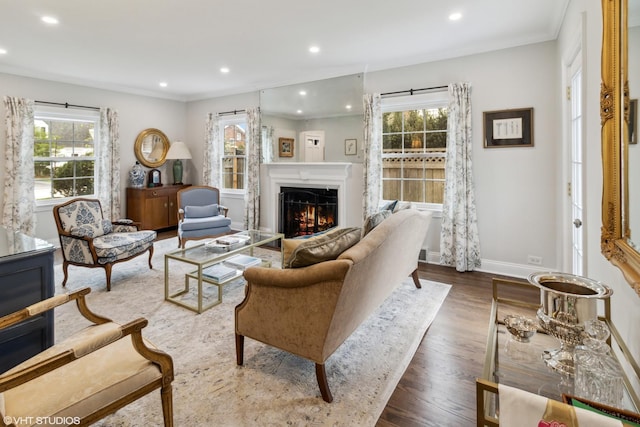 living area featuring plenty of natural light, recessed lighting, wood finished floors, a lit fireplace, and ornamental molding