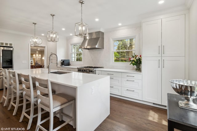 kitchen featuring a sink, wall chimney exhaust hood, a center island with sink, dark wood-style floors, and crown molding