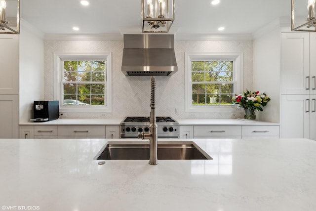 kitchen featuring wall chimney range hood, crown molding, decorative backsplash, white cabinetry, and stainless steel range