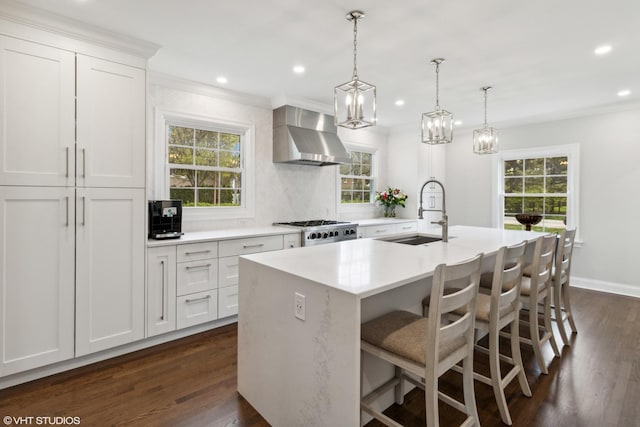 kitchen with a sink, wall chimney exhaust hood, a kitchen island with sink, light countertops, and dark wood finished floors