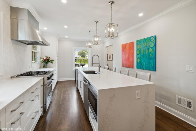 kitchen with high end stove, a sink, wall chimney exhaust hood, a kitchen island with sink, and dark wood-type flooring