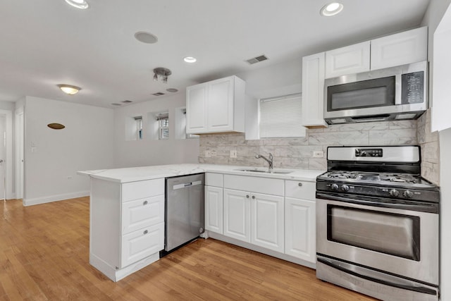kitchen featuring appliances with stainless steel finishes, a sink, a peninsula, white cabinets, and recessed lighting