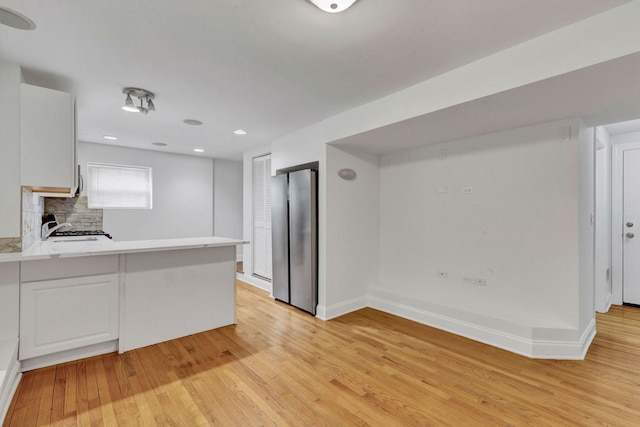 kitchen featuring freestanding refrigerator, a sink, light countertops, light wood-style flooring, and a peninsula