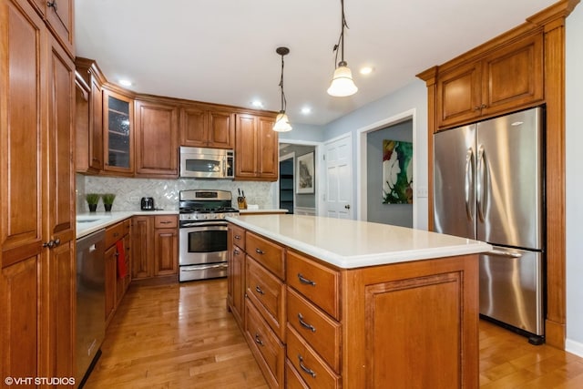 kitchen featuring appliances with stainless steel finishes, light wood finished floors, tasteful backsplash, a kitchen island, and light countertops