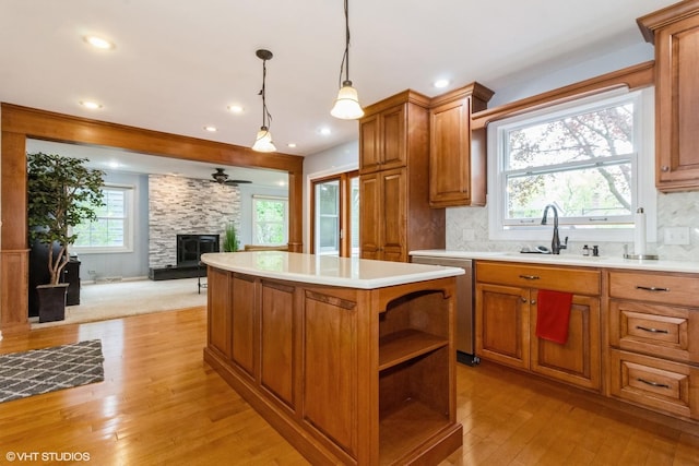 kitchen with stainless steel dishwasher, a sink, a center island, a stone fireplace, and light wood-style floors