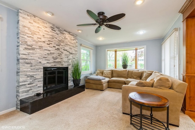 carpeted living room with crown molding, a stone fireplace, ceiling fan, and recessed lighting