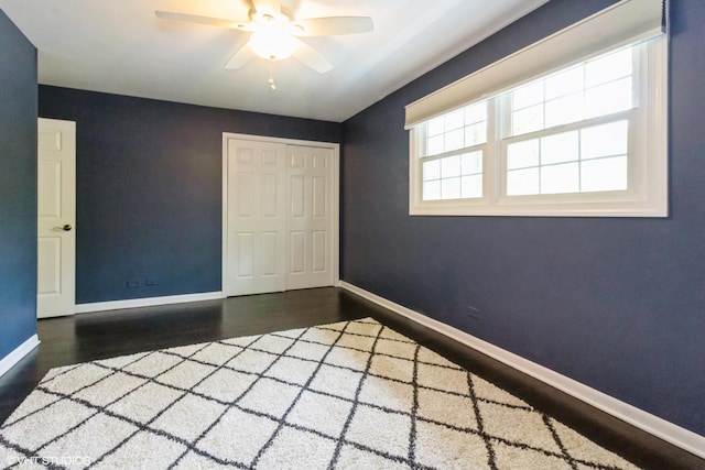 unfurnished bedroom with wood finished floors, a closet, baseboards, and ceiling fan