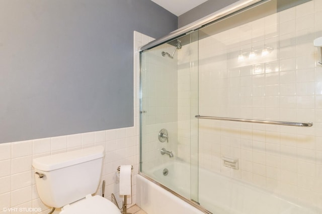 full bathroom featuring bath / shower combo with glass door, tile walls, toilet, and wainscoting