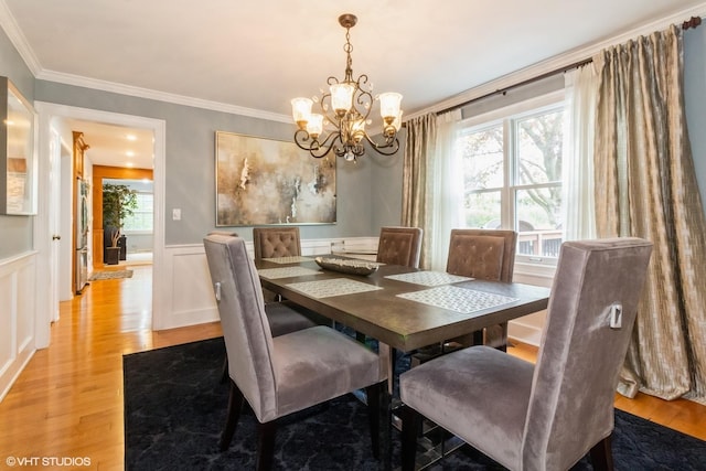 dining space with a chandelier, crown molding, light wood-type flooring, a wainscoted wall, and a decorative wall