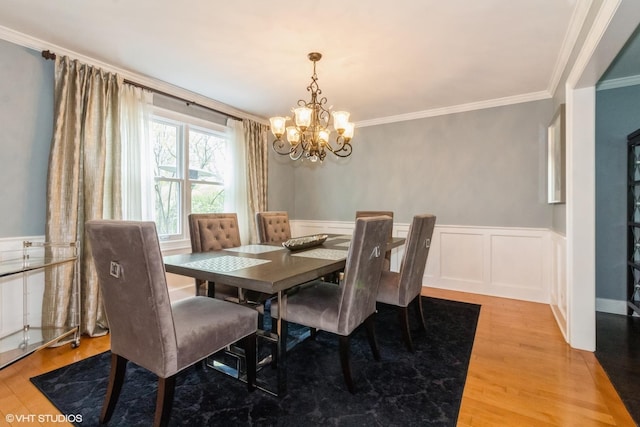 dining room with a chandelier, a wainscoted wall, crown molding, light wood finished floors, and a decorative wall