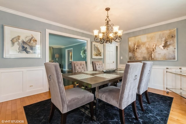 dining area with wood finished floors, a chandelier, ornamental molding, wainscoting, and a decorative wall