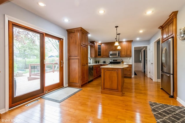 kitchen with appliances with stainless steel finishes, brown cabinetry, light countertops, a kitchen island, and light wood-type flooring