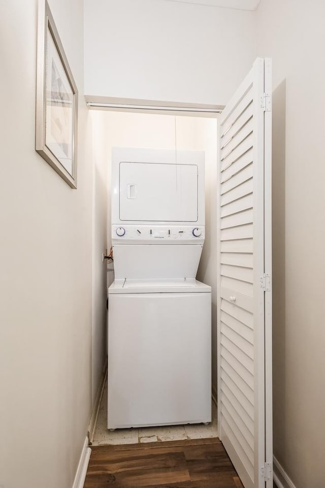 washroom with stacked washer / drying machine, wood finished floors, and baseboards