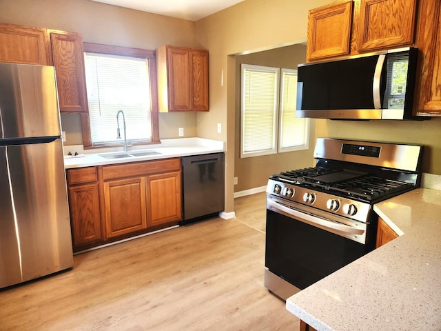 kitchen featuring appliances with stainless steel finishes, a sink, brown cabinetry, light wood-style floors, and baseboards