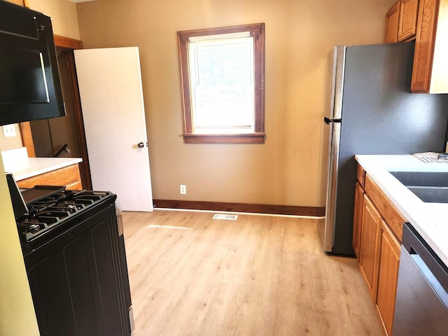 kitchen featuring appliances with stainless steel finishes, light wood finished floors, baseboards, light countertops, and brown cabinets