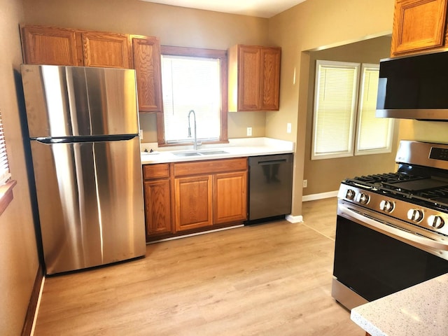 kitchen with stainless steel appliances, a sink, light countertops, baseboards, and light wood-type flooring