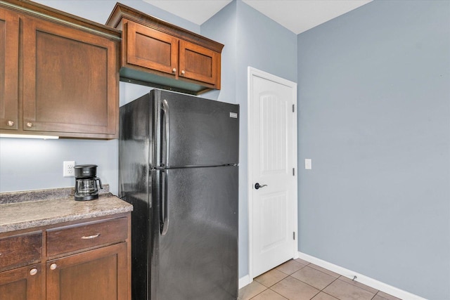 kitchen featuring freestanding refrigerator, light tile patterned flooring, and baseboards