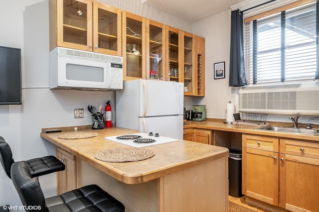 kitchen featuring white appliances, a breakfast bar, a peninsula, a sink, and glass insert cabinets