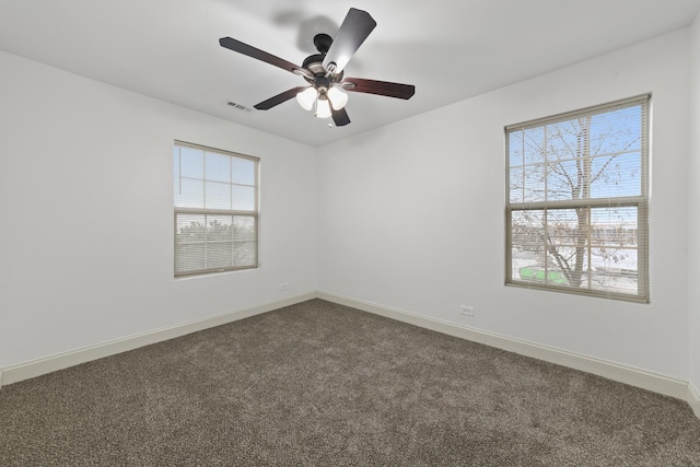 spare room featuring healthy amount of natural light, dark colored carpet, and baseboards