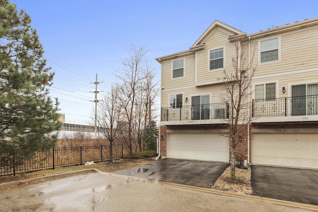 view of front of property featuring driveway, fence, brick siding, and an attached garage