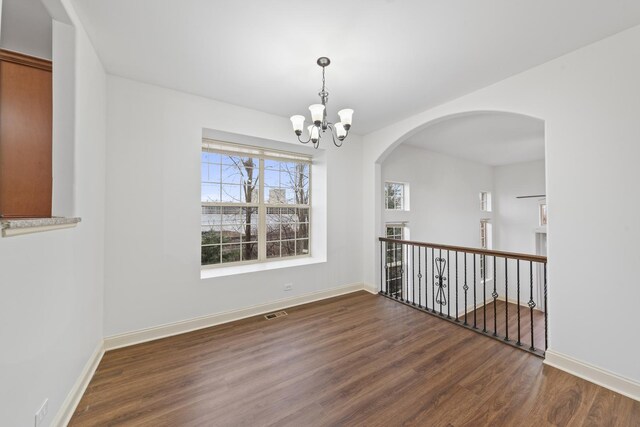 spare room featuring wood finished floors, a chandelier, arched walkways, and baseboards