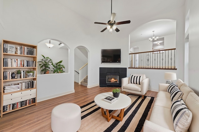 living area featuring wood finished floors, a tile fireplace, a ceiling fan, and stairway
