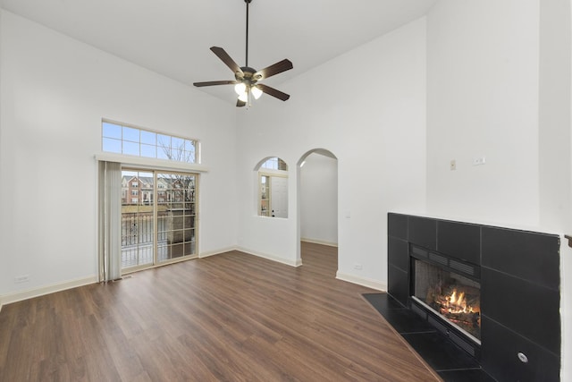 unfurnished living room featuring wood finished floors, a tiled fireplace, high vaulted ceiling, a ceiling fan, and baseboards