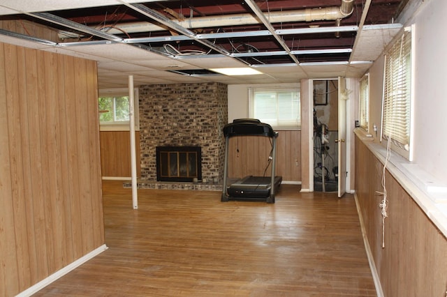workout area featuring wood finished floors, a brick fireplace, wood walls, and baseboards