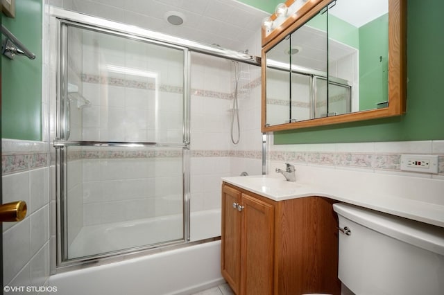 full bathroom with tile walls, combined bath / shower with glass door, vanity, a wainscoted wall, and toilet