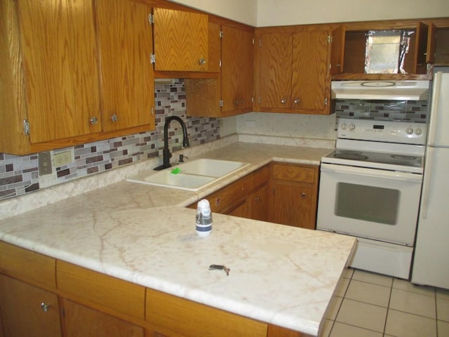 kitchen with white appliances, a sink, under cabinet range hood, light countertops, and brown cabinetry