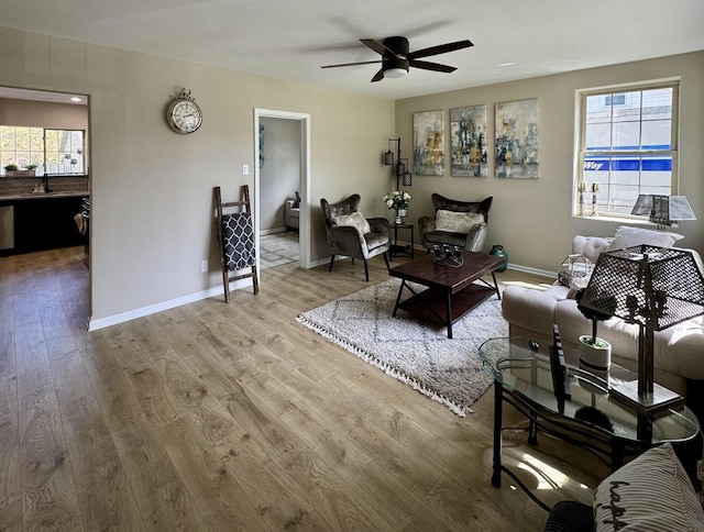 living area with wood finished floors, a ceiling fan, healthy amount of natural light, and baseboards