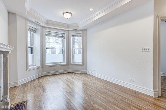 empty room featuring crown molding, wood finished floors, a tray ceiling, baseboards, and ornate columns