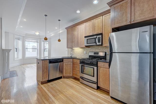 kitchen featuring stainless steel appliances, a peninsula, light wood finished floors, decorative backsplash, and pendant lighting