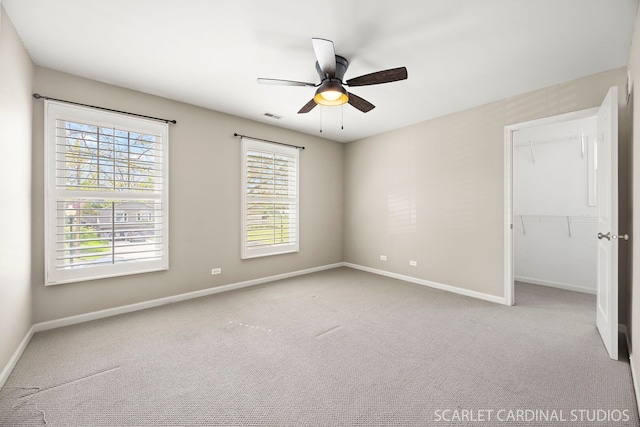 unfurnished bedroom featuring baseboards, carpet floors, a spacious closet, a ceiling fan, and a closet