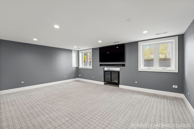 unfurnished living room featuring carpet floors, recessed lighting, baseboards, a glass covered fireplace, and plenty of natural light