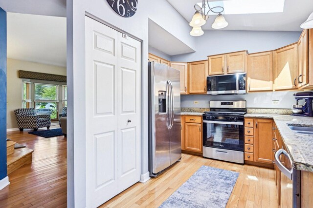 kitchen featuring appliances with stainless steel finishes, light wood-style flooring, light stone counters, lofted ceiling, and a chandelier