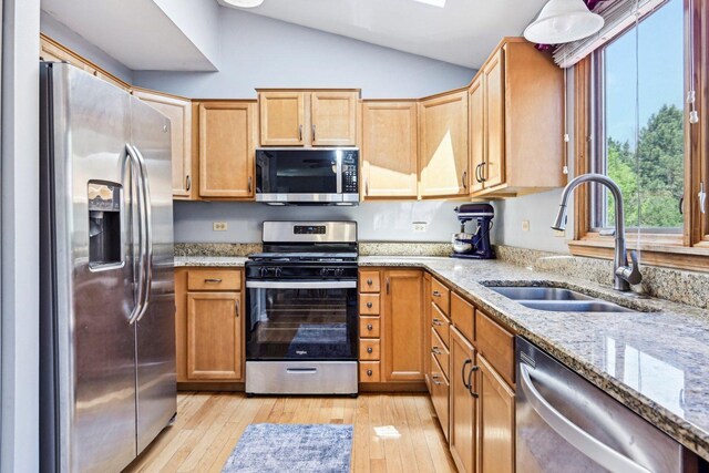 kitchen with appliances with stainless steel finishes, a sink, lofted ceiling, light wood-style floors, and light stone countertops