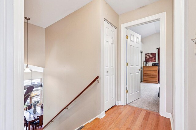 hallway featuring an upstairs landing, light wood finished floors, and baseboards