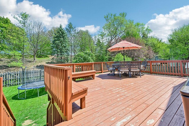 wooden terrace with outdoor dining area, a trampoline, and view of wooded area