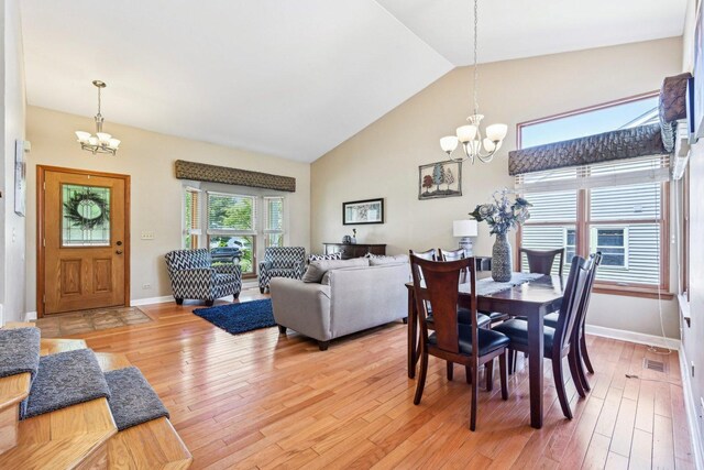 dining room with a chandelier, high vaulted ceiling, light wood finished floors, and baseboards