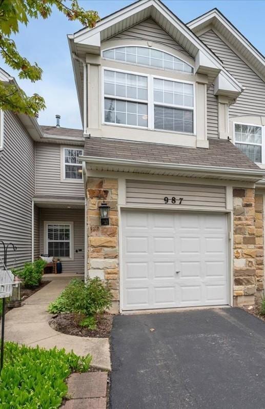 view of front of home with stone siding, a garage, asphalt driveway, and roof with shingles