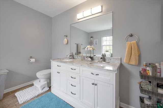 bathroom with baseboards, toilet, double vanity, and wood finished floors