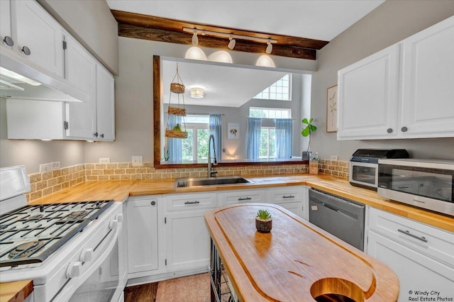 kitchen featuring butcher block countertops, stainless steel appliances, a sink, beamed ceiling, and white cabinetry