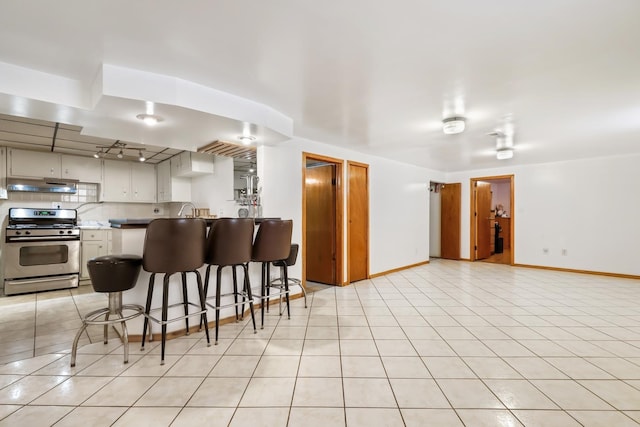 kitchen featuring gas stove, under cabinet range hood, a peninsula, a breakfast bar area, and light tile patterned floors