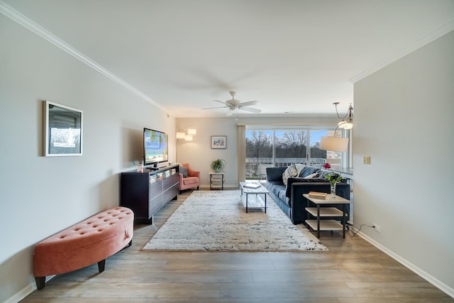 living area featuring ornamental molding, wood finished floors, ceiling fan, and baseboards