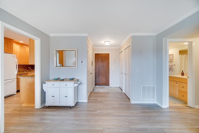 corridor with light wood-style flooring, crown molding, a sink, and baseboards