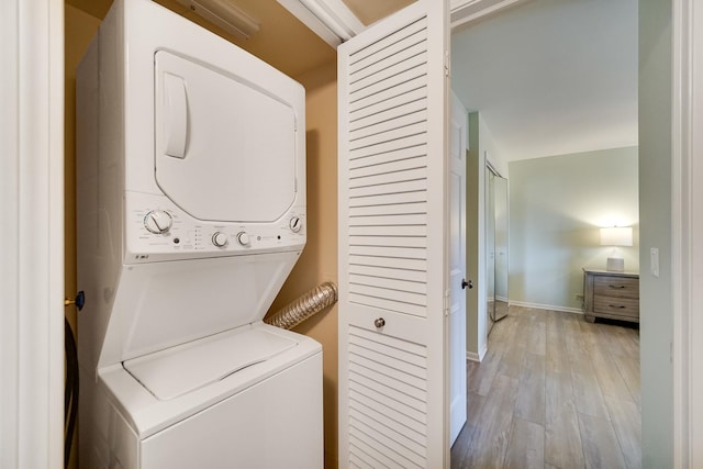 laundry room featuring stacked washer / drying machine, wood finished floors, and baseboards